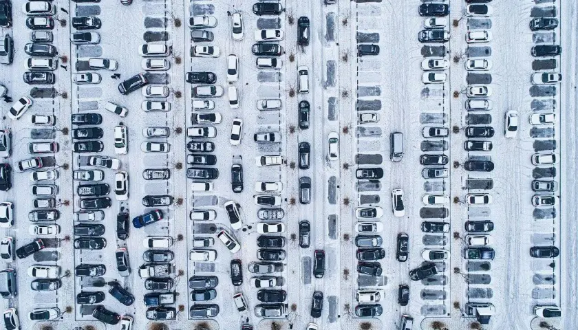 Zimowy parking z wieloma samochodami. Wygląda, jakby druga rata OC po terminie, bo tyle aut stoi w śniegu.