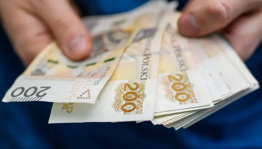 Dłonie trzymające plik banknotów 200 zł. Może to być związane z zajęciem komorniczym, gdy pieniądze są przekazywane.