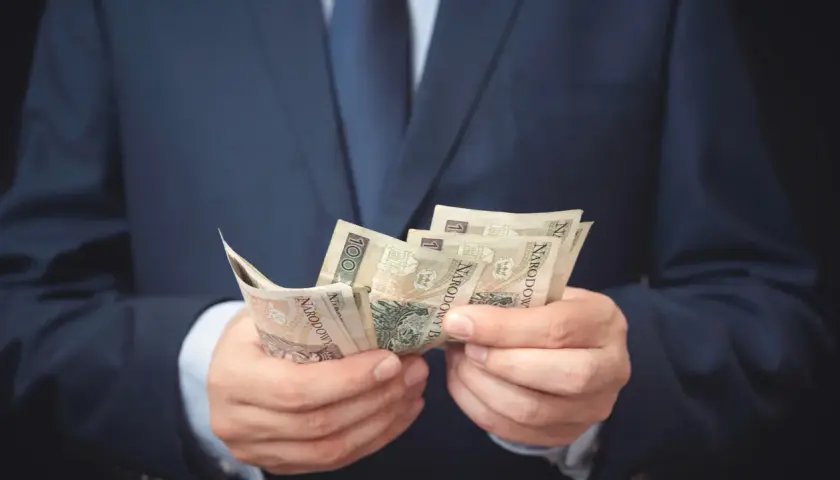 Mężczyzna w garniturze liczy banknoty. Może to symbolizować otrzymanie odszkodowania i zadośćuczynienia po trudnym zdarzeniu.