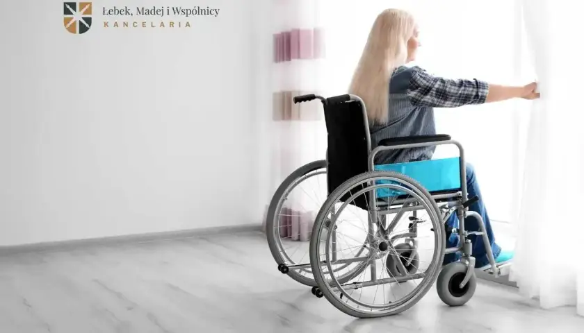 Kobieta na wózku inwalidzkim, symbol trwałego uszczerbku na zdrowiu, patrzy przez okno.
