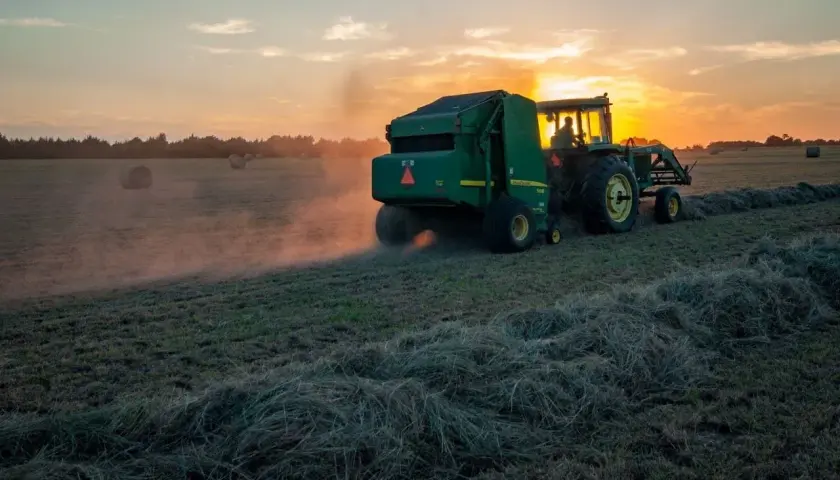 Traktor z prasą zbiera siano o zachodzie słońca. Dbałość o ubezpieczenie rolnicze zapewnia spokój ducha.