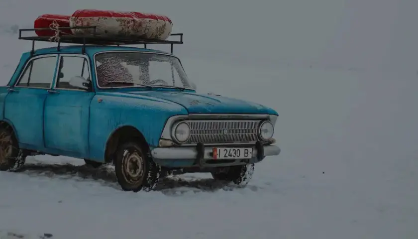 Niebieski, stary samochód z bagażem na dachu stoi na śniegu. Widać, że to auto z czasów PRL-u, do jakiego wieku auta jeździli Polacy.