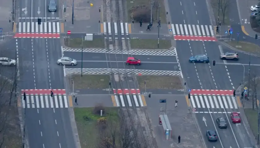 Skrzyżowanie z przejściami dla pieszych. Czerwony samochód wykonuje wyprzedzanie na pasach, ignorując pieszych.