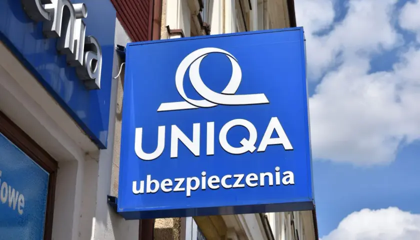 Niebieski szyld z logo i napisem "UNIQA ubezpieczenia". Firma UNIQA oferuje ubezpieczenia.