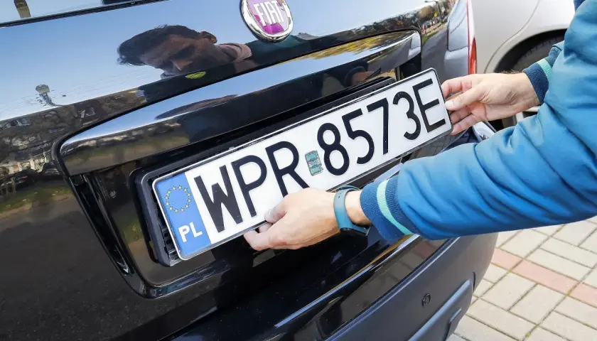 Ręce montują tablicę rejestracyjną. Uniknięcie mandatu za brak tablicy rejestracyjnej jest ważne.