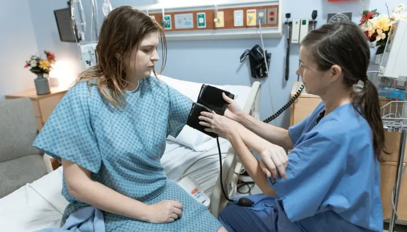 Pielęgniarka mierzy ciśnienie pacjentce w szpitalnej sali. To przykład zdarzenia medycznego, które wymaga obserwacji.