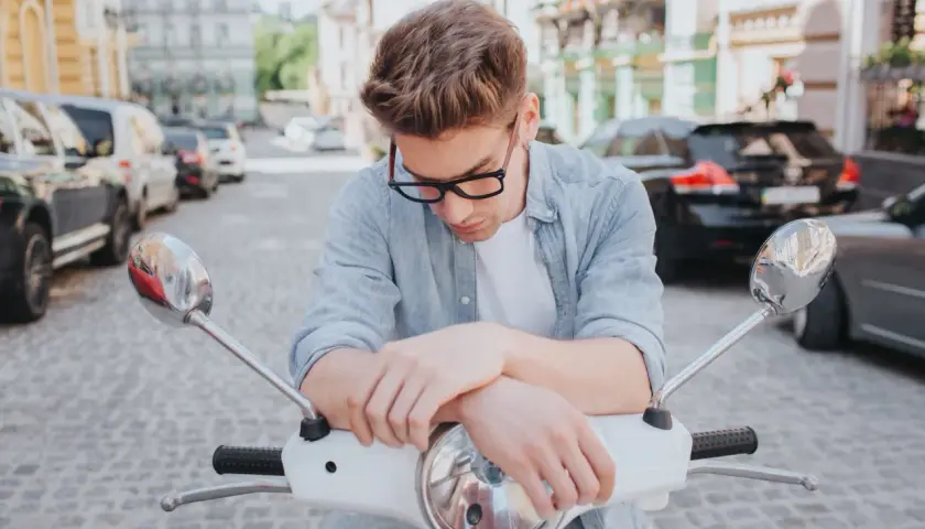 Młody mężczyzna na skuterze, zamyślony. Pomyśl o ubezpieczeniu motoroweru, by podróżować bez obaw.