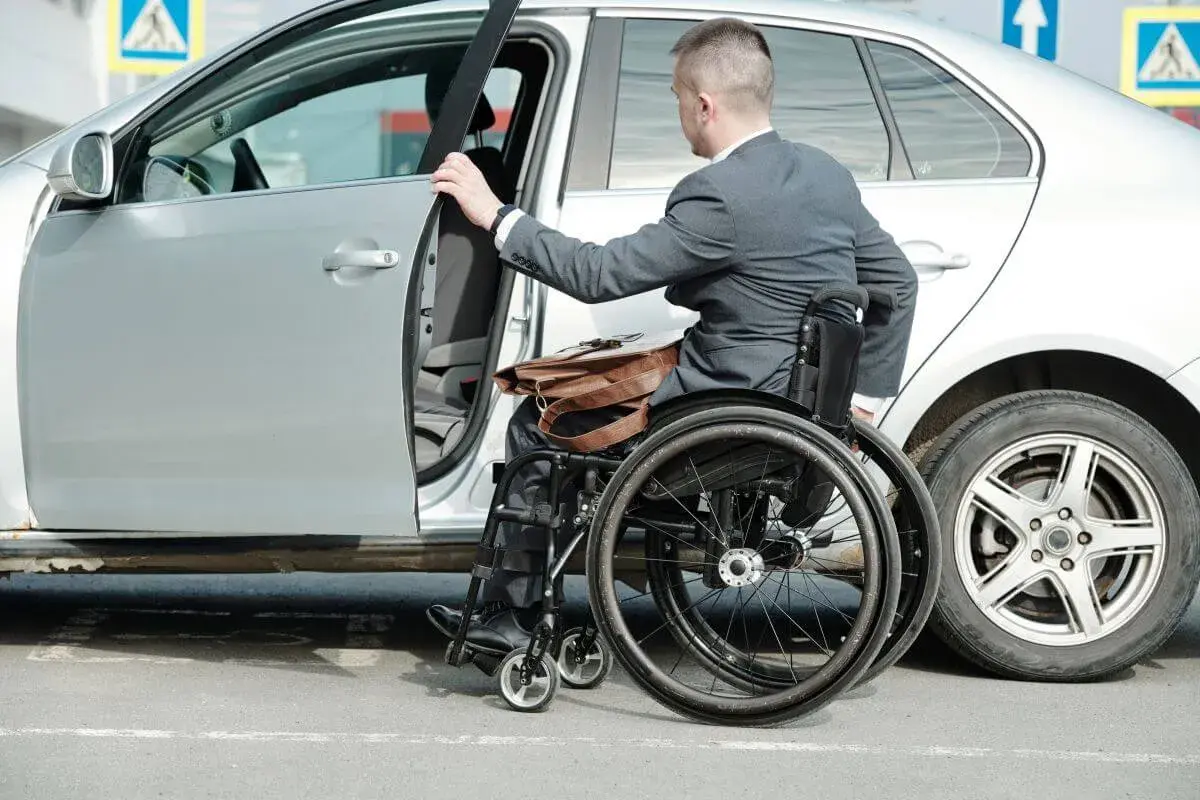 Mężczyzna na wózku inwalidzkim wsiada do samochodu. Ubezpieczenie samochodu a stopień niepełnosprawności to ważna kwestia dla osób z niepełnosprawnościami.