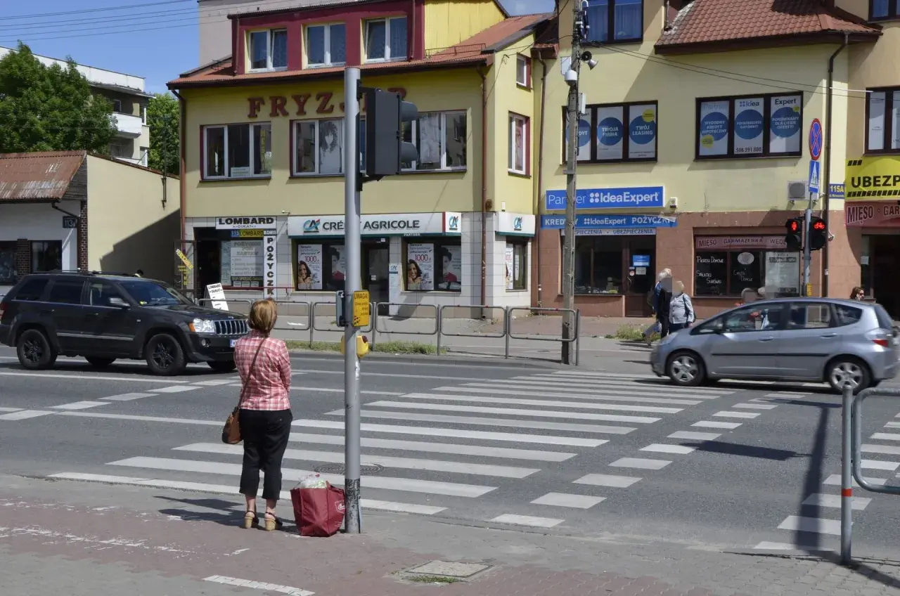 Kobieta czeka na zielone światło na pasach, kiedy należy zachować szczególną ostrożność. Samochody zbliżają się do przejścia.