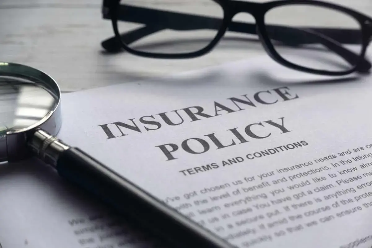 Okulary, lupa i dokument "Insurance Policy" symbolizują analizę polisy PZU po śmierci teścia.