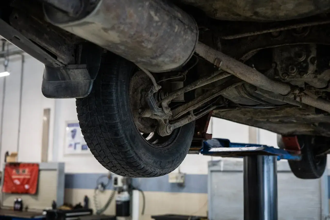 Podnośnik samochodowy ukazuje podwozie auta, gdzie widać koło i elementy zawieszenia. Może to być etap przygotowań do zwrotu autocasco po sprzedaży samochodu.