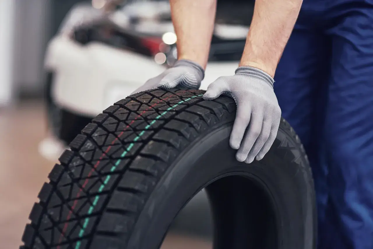 Mechanik w rękawiczkach trzyma oponę zimową. Czy w Polsce jest obowiązek zmiany opon na zimowe? Odpowiedź brzmi: nie.