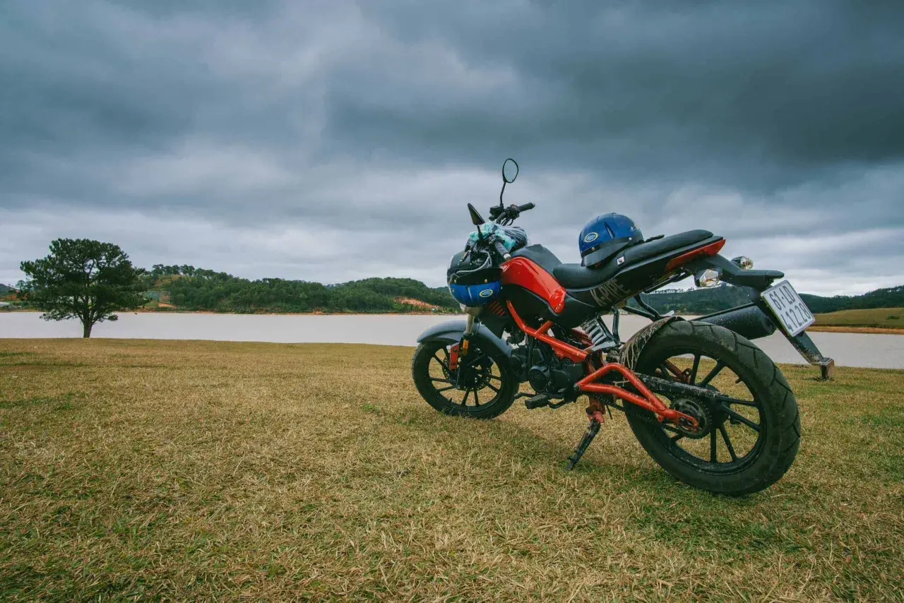 Czerwono-czarny motocykl z niebieskim kaskiem na siedzeniu, gotowy do jazdy nad jeziorem.