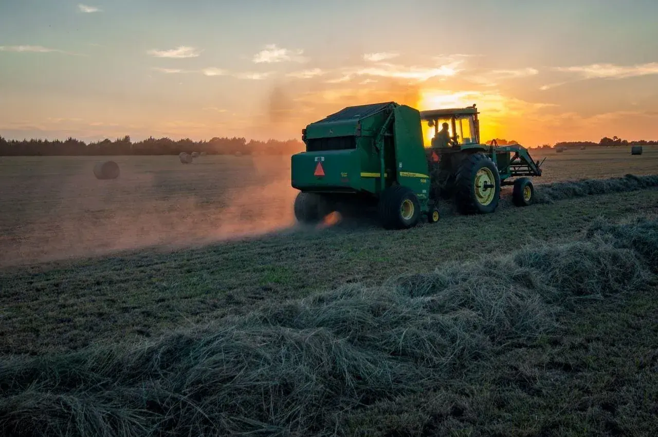 Traktor z prasą zbiera siano o zachodzie słońca. Dbałość o ubezpieczenie rolnicze zapewnia spokój ducha.