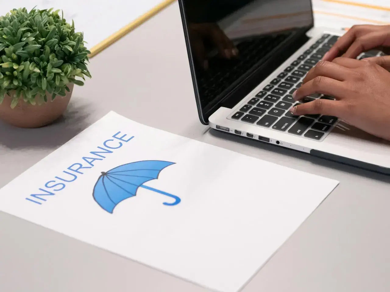 Przerwa w posiadaniu samochodu a zniżki na ubezpieczenie. Na biurku dokument "Insurance" z parasolką i osoba pisząca na laptopie.