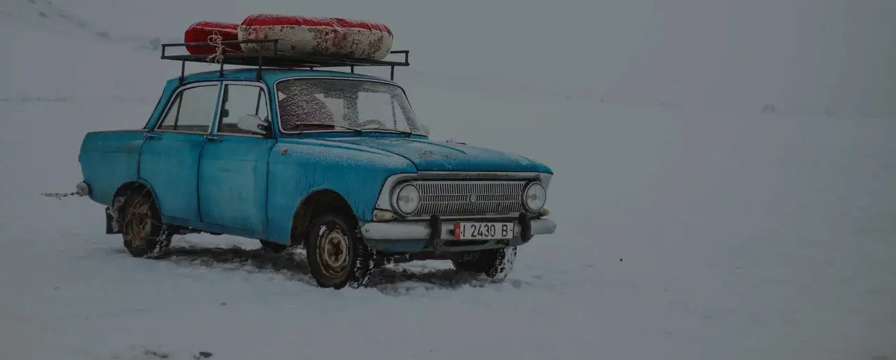 Niebieski, stary samochód z bagażem na dachu stoi na śniegu. Widać, że to auto z czasów PRL-u, do jakiego wieku auta jeździli Polacy.