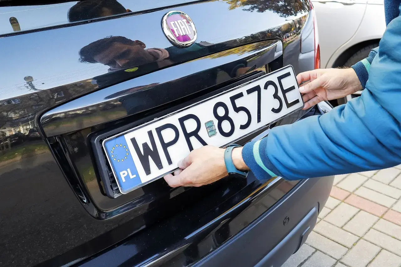 Ręce montują tablicę rejestracyjną. Uniknięcie mandatu za brak tablicy rejestracyjnej jest ważne.