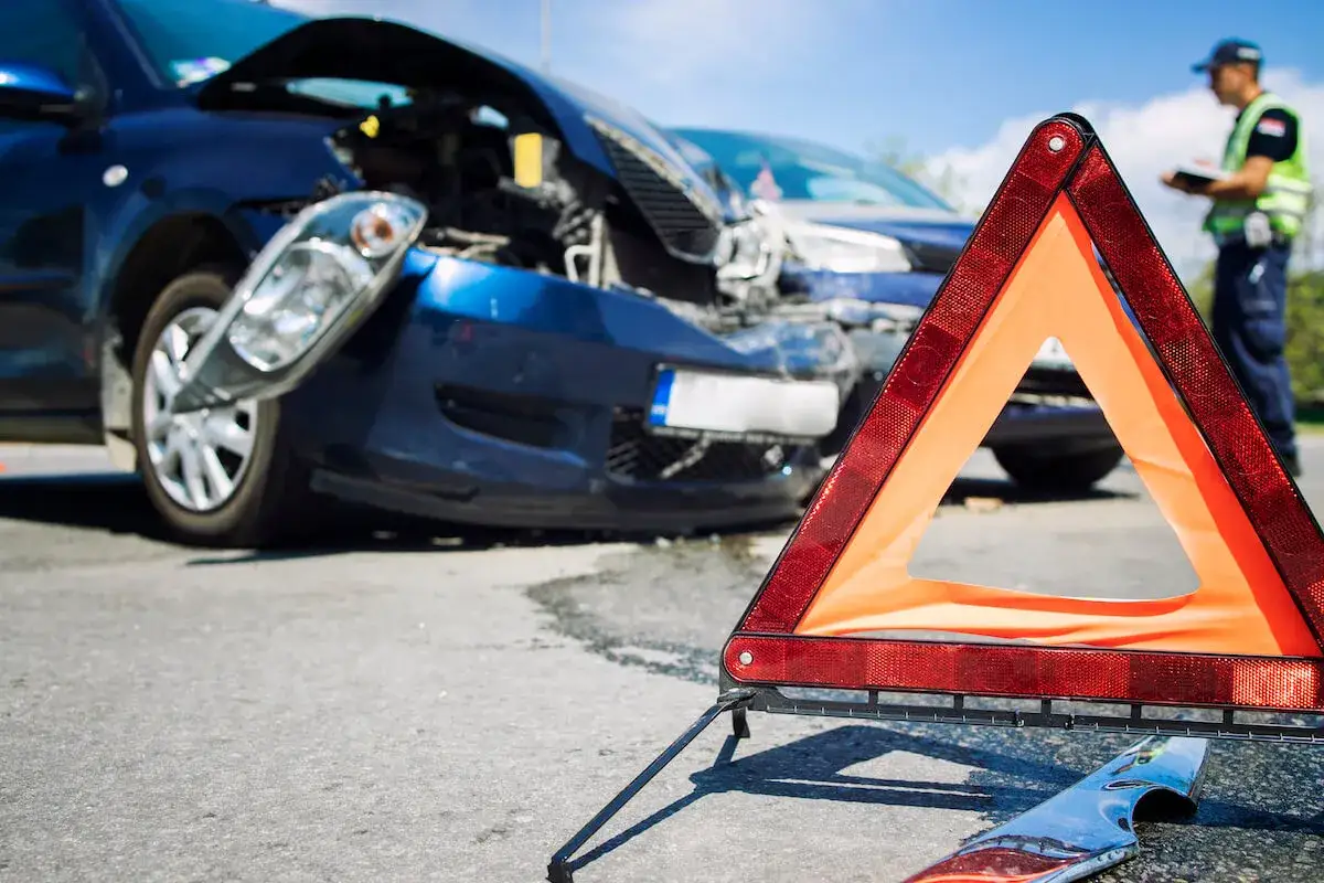 Trójkąt ostrzegawczy przed uszkodzonymi autami. Policjant spisuje zeznania po zdarzeniu, które mogło być próbą ucieczki z miejsca wypadku.