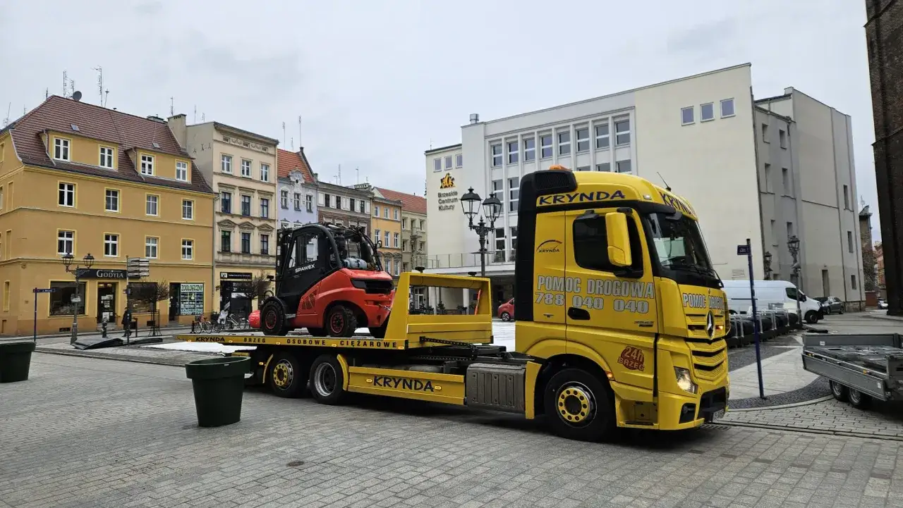 Żółta ciężarówka pomocy drogowej KRYNDA z wózkiem widłowym na lawecie. Usługa mtu assistance.