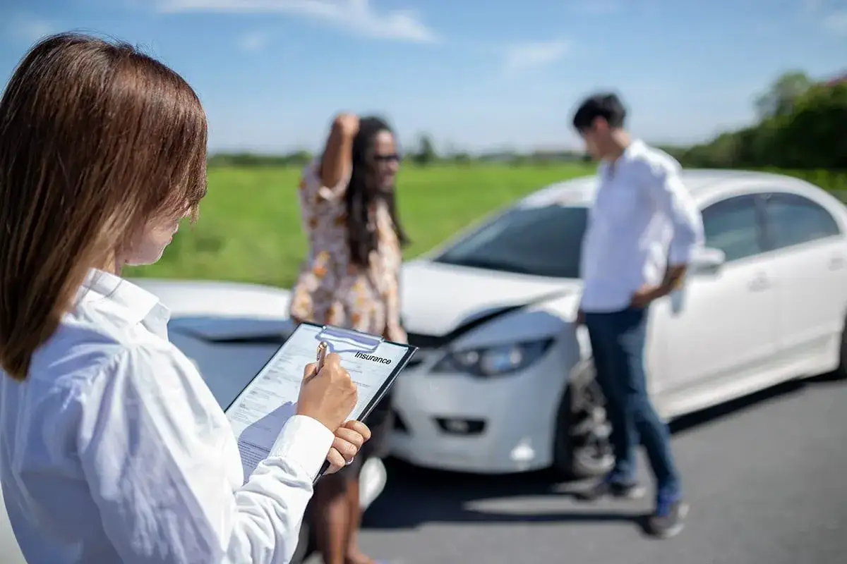 Ubezpieczyciel spisuje protokół po wypadku, zgodnie z art. 34 ustawy o ubezpieczeniach obowiązkowych. W tle uszkodzone auto i uczestnicy zdarzenia.