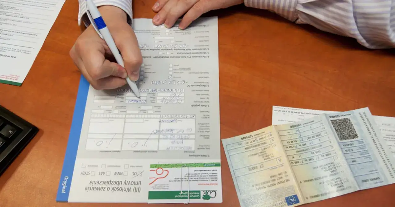 Ręka wypełnia wniosek o ubezpieczenie, szukając sposobów na tanie OC. Obok dokumenty pojazdu.
