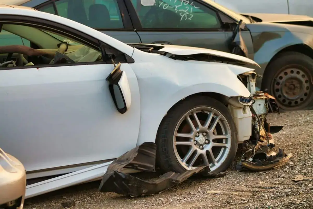 Uszkodzone białe auto po wypadku, lusterko urwane, zderzak zniszczony. Potrzebna ochrona zniżek AC.
