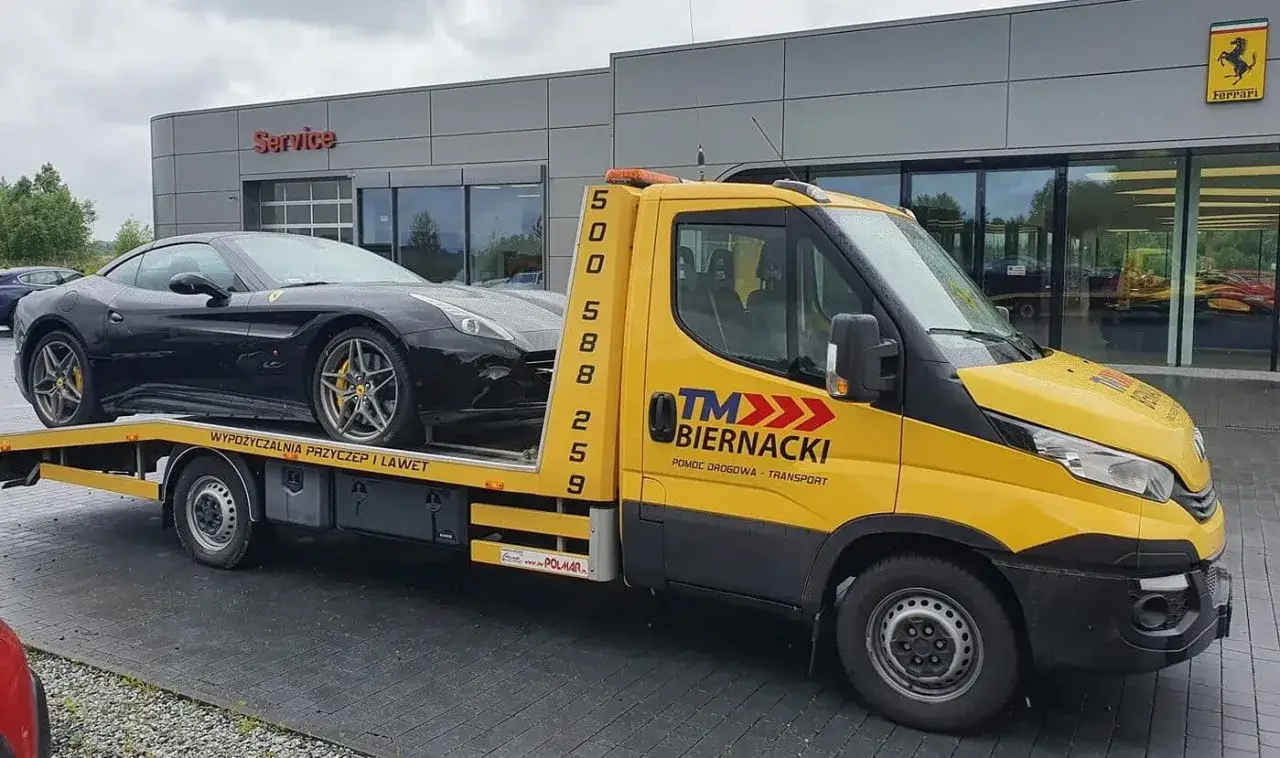Żółta laweta z logo TM Biernacki zapewnia pomoc drogową dla czarnego Ferrari.
