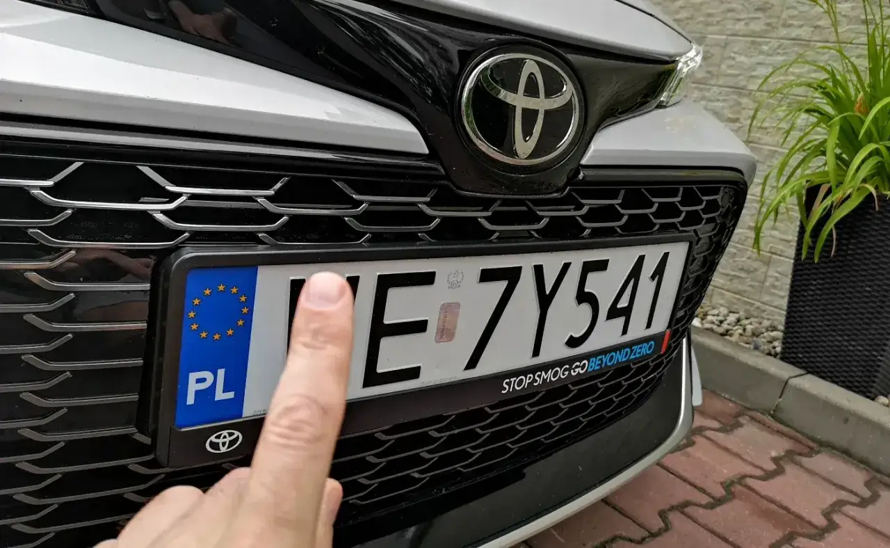 Palec wskazuje na tablicę rejestracyjną samochodu. Brak tablicy to potencjalny mandat.