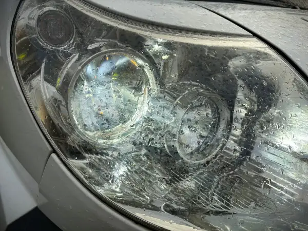 Krople deszczu na reflektorze, który świeci, sugerują jazda bez jednego światła.